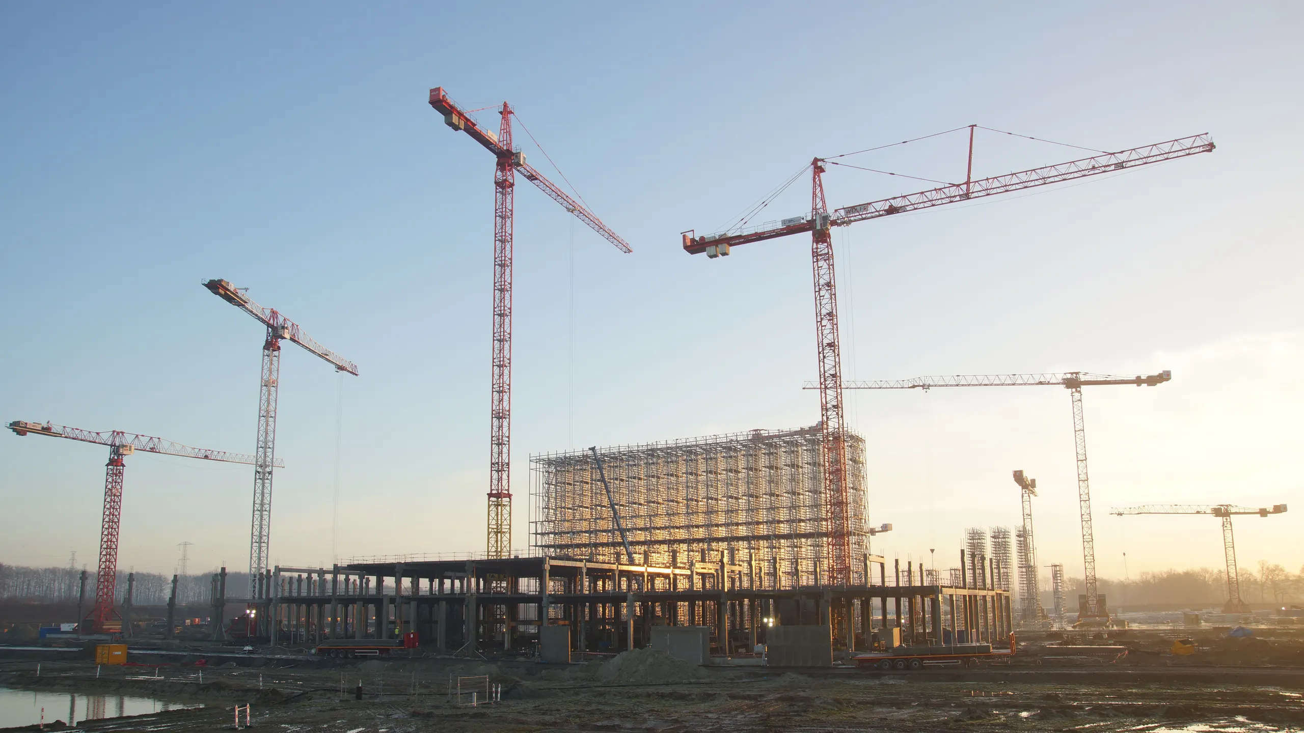Tower cranes over a commercial building under construction at sunrise